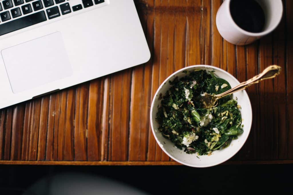 Overhead of bowl of kale coffee and laptop on desk