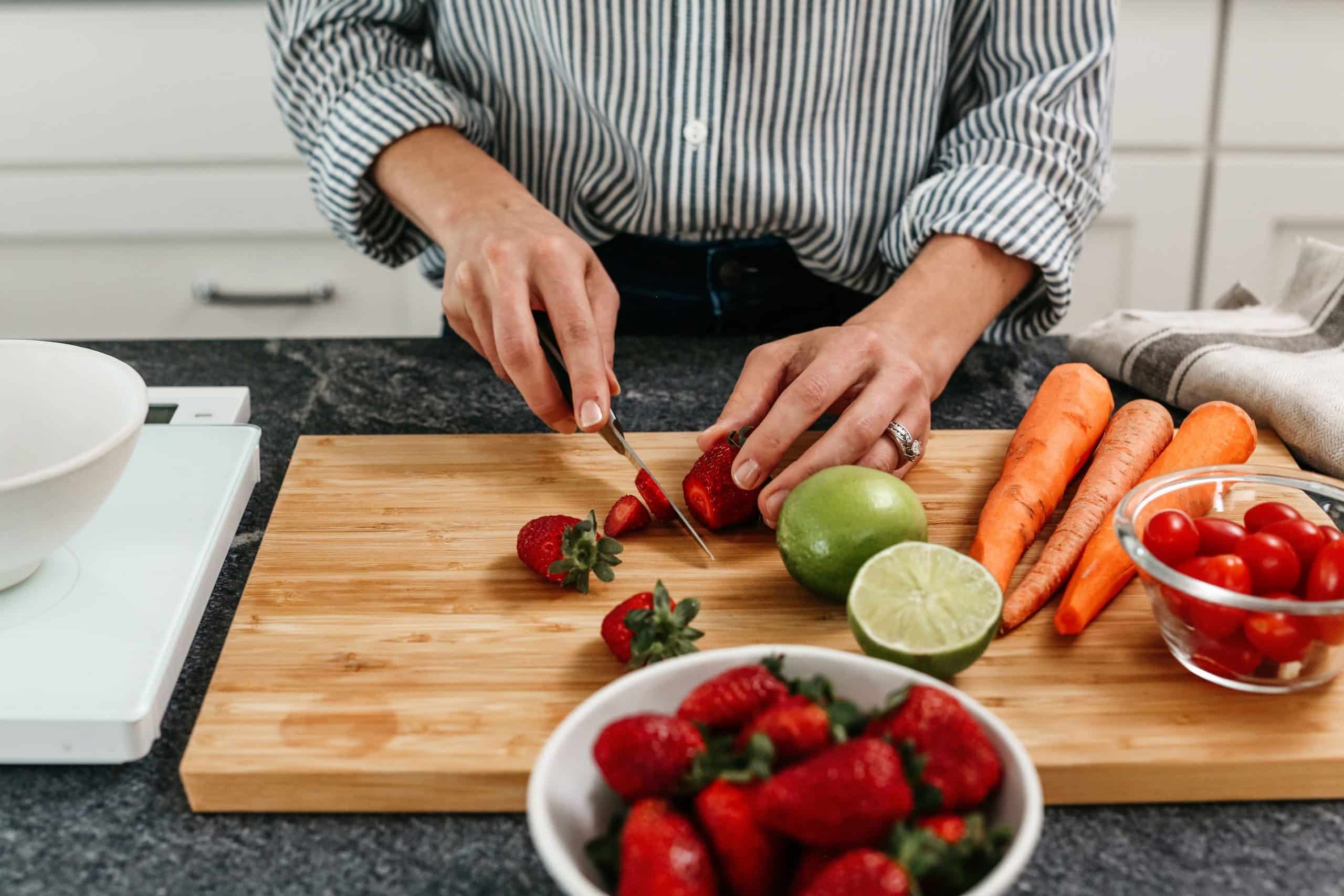 Person cutting strawberries on cutting board with other vegetables and fruit